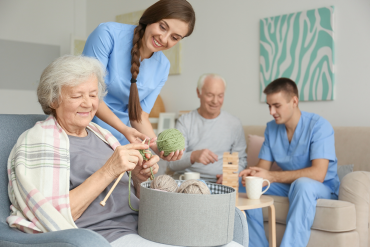 Two Seagrape Home Health Care aides assisting a senior husband and wife with knitting and gameplay