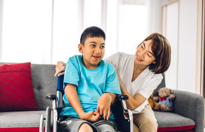 Portrait of enjoy happy love family asian mother playing and carer helping look at disabled son child sitting in wheelchair moments good time at home.disability care concept